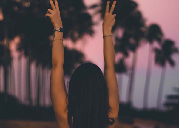 Frau streckt die Hände in die Luft bei Sonnenuntergang